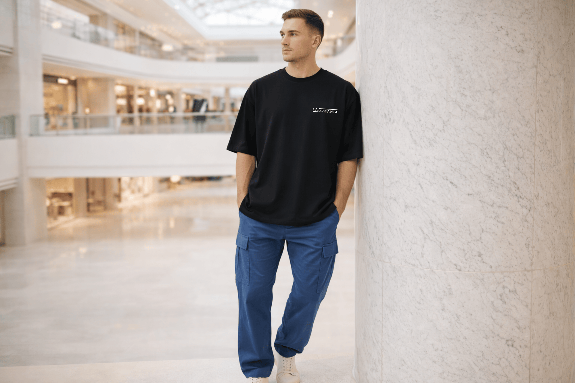 LaUrbania Jet Black oversized t-shirt model standing in luxury mall hands in pocket leaning marble wall